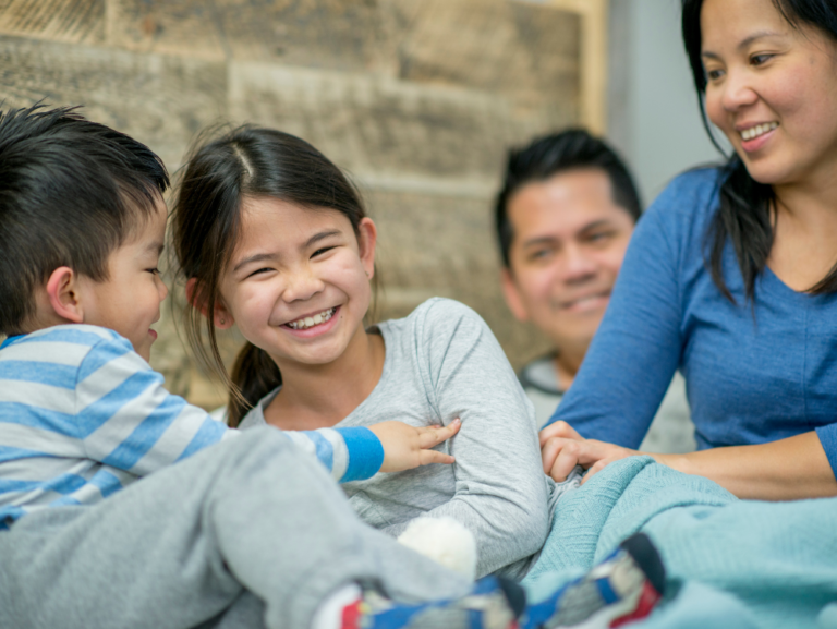 A family of four is sitting together and the two kids are playing and laughing with each other.